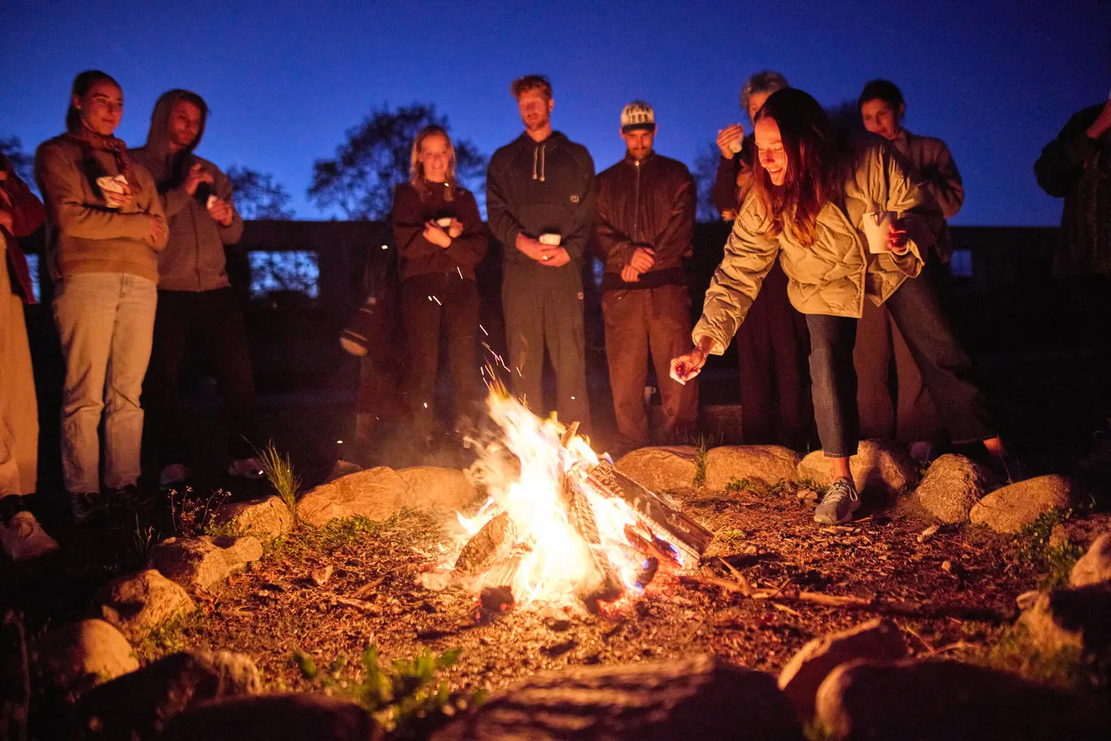 A group standing around a fire at dusk.